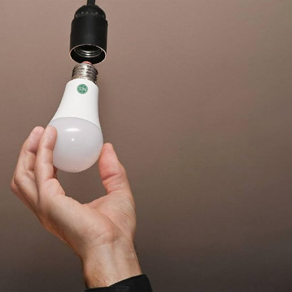 Hand holding a NJS LED light bulb against a plain background